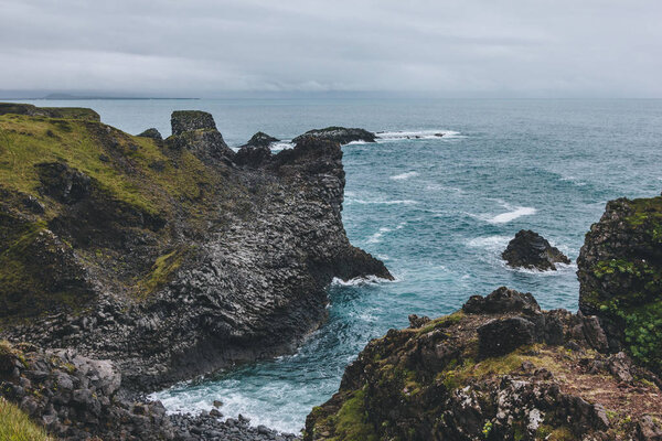 scenic view of beautiful cliffs in front of blue ocean in Arnarstapi, Iceland on cloudy day