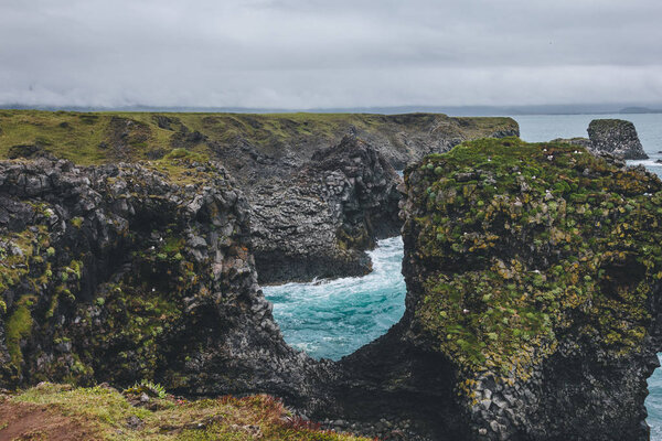 beautiful mossy cliffs in front of blue ocean in Arnarstapi, Iceland on cloudy day