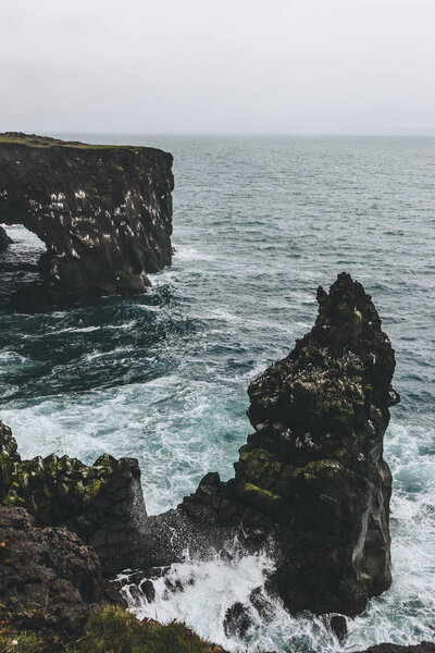 beautiful rocky cliffs and stormy ocean in Arnarstapi, Iceland on cloudy day