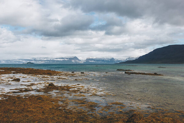 scenic shot of lake shore in Iceland with snowy mountains on background