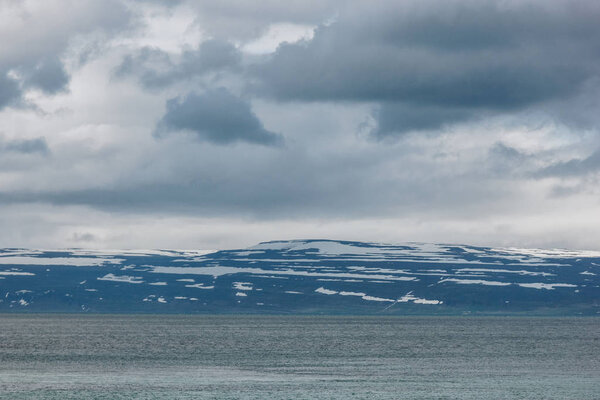 dramatic shot of lake under cloudy sky in Iceland with snowy mountains on background