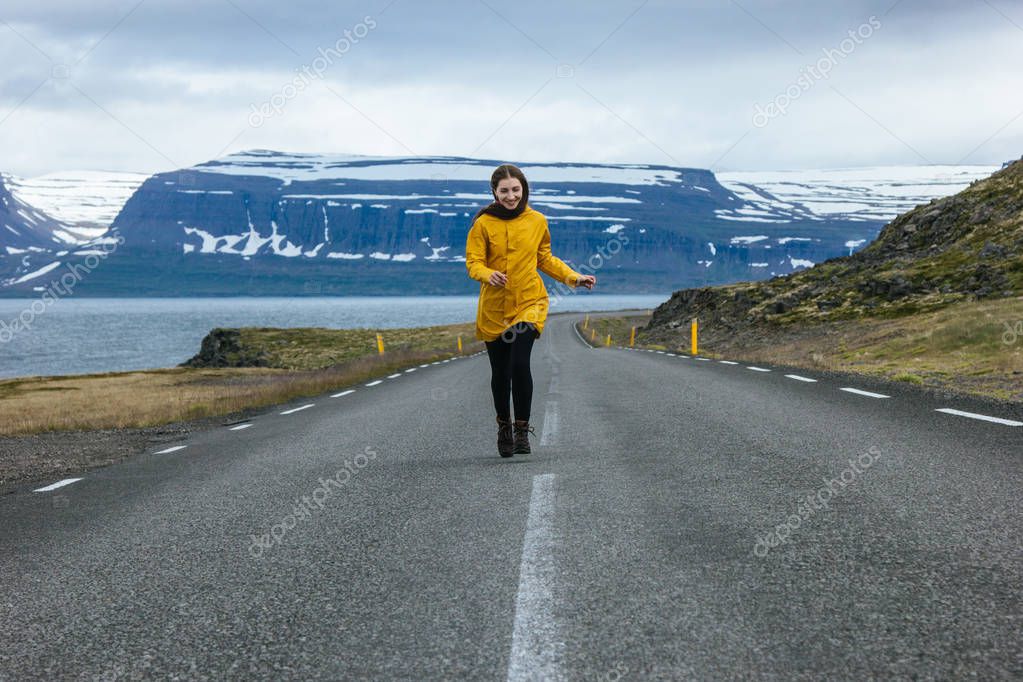 Young woman running by empty road in iceland with beautiful mountains and lake on background