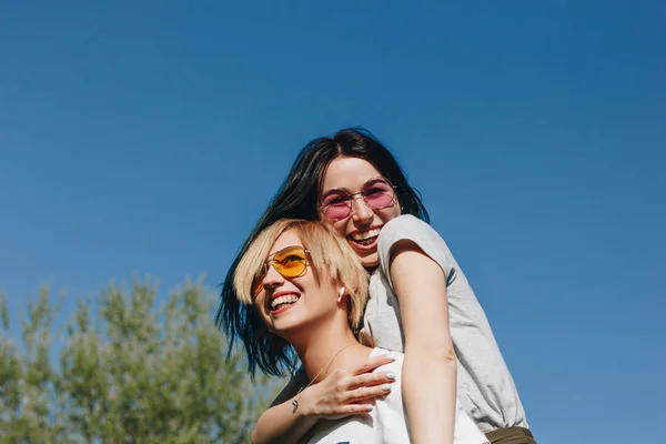 Vista inferior de las mujeres jóvenes riendo abrazándose delante del cielo azul - foto de stock