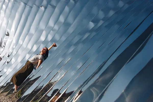 WROCLAW, POLONIA - 18 MAYO 2018: mujer joven y relajada frente a la escultura hecha de material reflectante - foto de stock