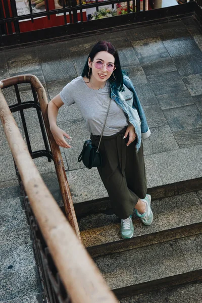 Vue grand angle de la jeune femme élégante debout sur les escaliers et regardant la caméra — Photo de stock