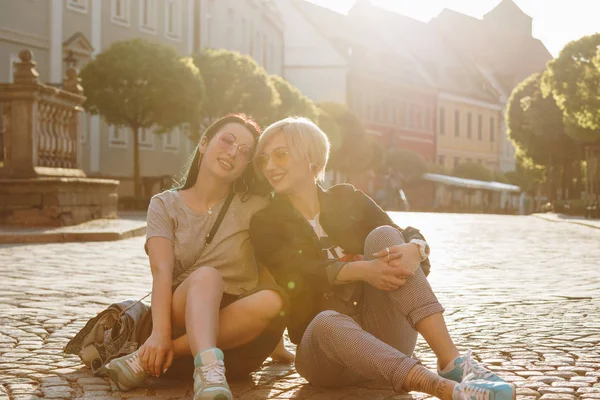 Hermosas mujeres jóvenes sentadas en la calle empedrada juntas al atardecer - foto de stock