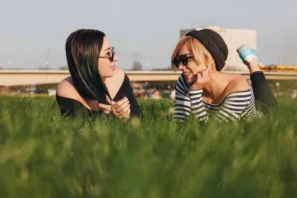 Felices mujeres jóvenes tumbadas en la hierba en el parque y charlando - foto de stock