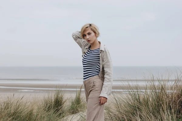 Mujer joven con estilo en camisa a rayas y chaqueta en la orilla arenosa - foto de stock