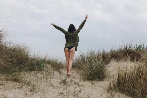 Vue arrière de la jeune femme sur une dune de sable sous un ciel nuageux — Photo de stock