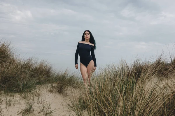 Jovem mulher atraente em bodysuit preto na duna de areia sob céu nublado — Fotografia de Stock
