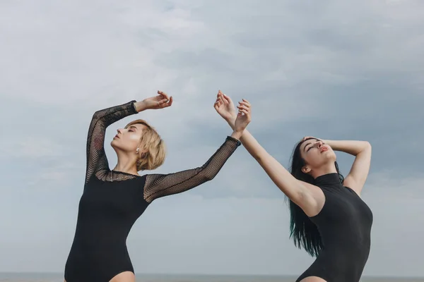 Sensuales mujeres jóvenes en trajes negros bailando frente al cielo nublado - foto de stock