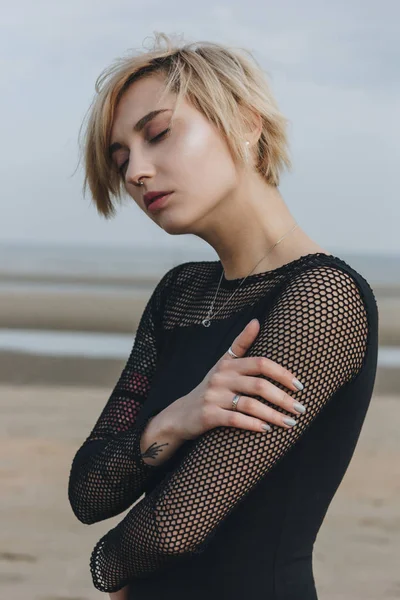 Sensual mujer joven en camisa negra en frente de la orilla del mar en día nublado - foto de stock