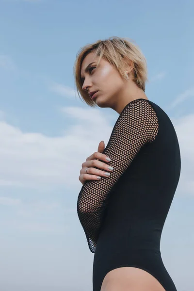 Sensual young woman in black bodysuit in front of cloudy sky — Stock Photo