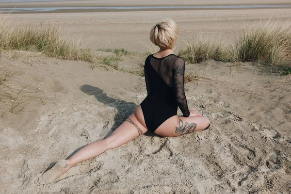 Joven mujer en traje de cuerpo practicando yoga en una pata rey paloma pose en duna arenosa - foto de stock
