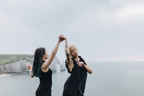Молодые женщины держатся за руки на скале перед океаном в облачный день — стоковое фото