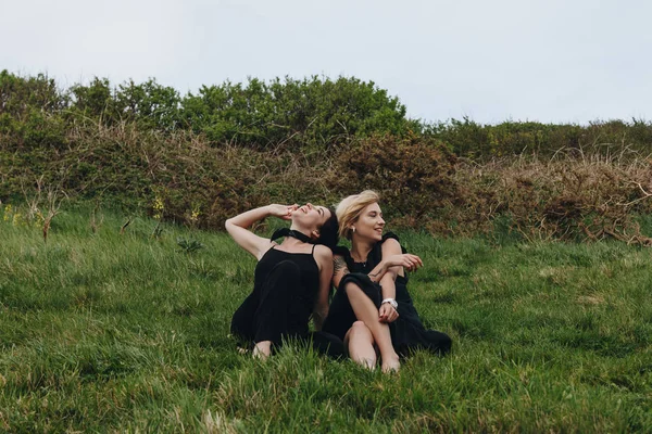 Feliz jóvenes mujeres en negro relajarse en verde prado - foto de stock