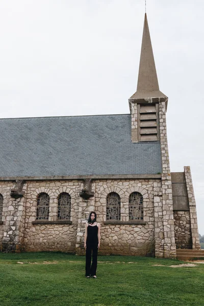 Приваблива молода жінка стоїть на зеленій траві перед старовинною церквою — стокове фото