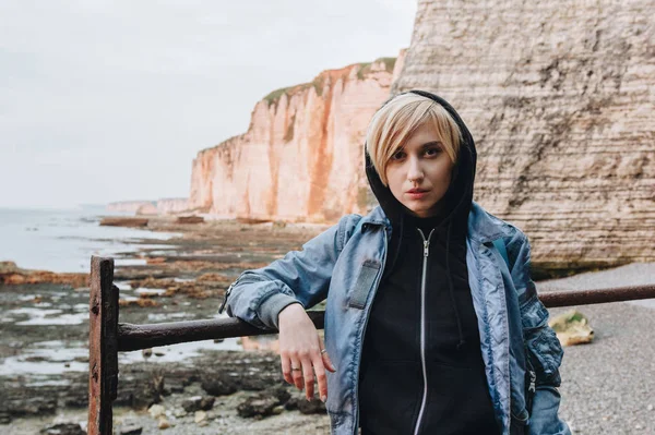 Hermosa mujer joven de pie frente a acantilados rocosos en la orilla del mar - foto de stock