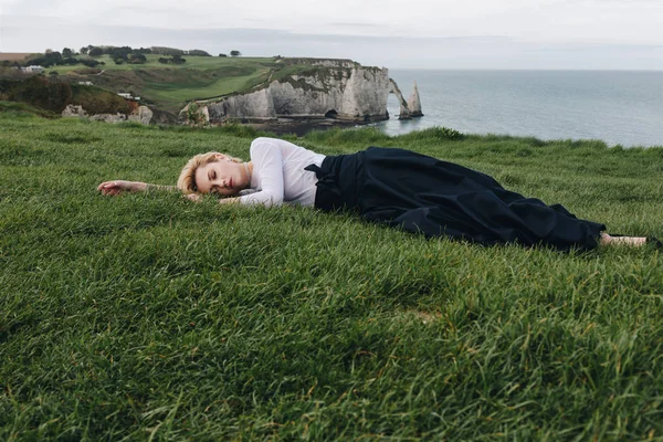 Jolie fille couchée sur l'herbe verte sur la falaise, Etretat, Normandie, France — Photo de stock