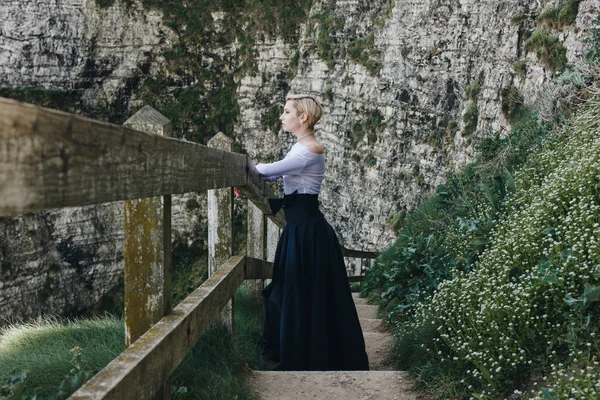 Elegante chica posando en las escaleras con barandillas de madera en acantilado rocoso, Etretat, Normandía, Francia - foto de stock