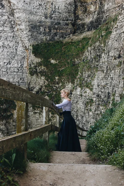 Красива дівчина стояла на сходи з дерев'яними поручнями на кам'янистій скелі, Етрета, Нормандія, Франція — стокове фото