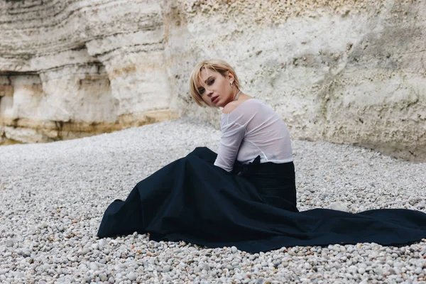 Atractiva chica sentada en la orilla cerca del acantilado, Etretat, Normandía, Francia - foto de stock