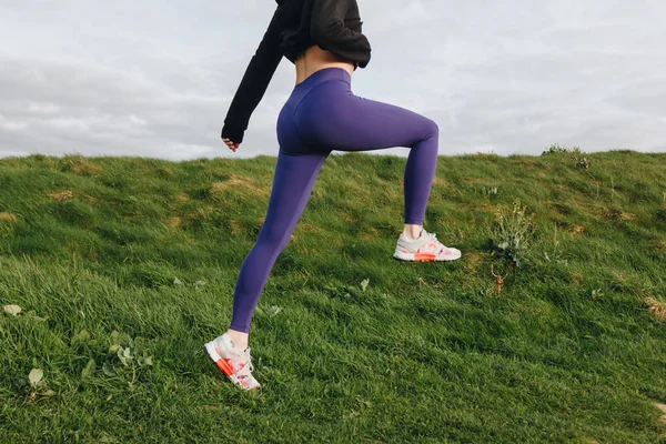 Vista recortada de la mujer atlética en ropa deportiva elegante ejercicio sobre hierba verde, Etretat, Francia - foto de stock