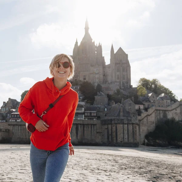 Bella ragazza allegra in felpa rossa con cappuccio posa vicino al monte Saint Michael, Francia — Foto stock