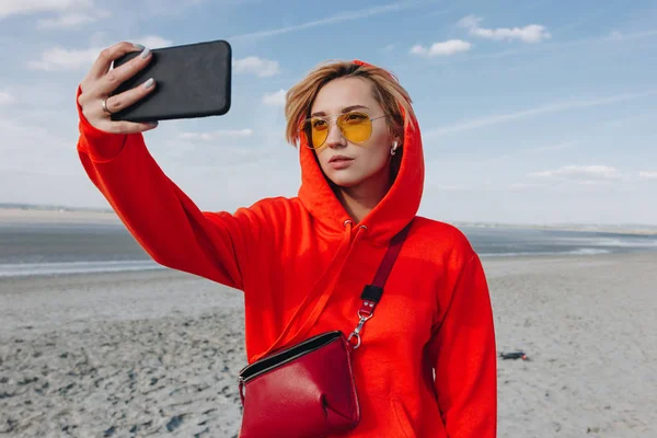 Hermosa chica en sudadera con capucha roja tomar selfie en la playa, monte de San Miguel, Francia - foto de stock