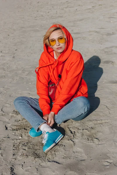 Stylish girl in red hoodie sitting on sandy beach, Saint michaels mount, Normandy, France — Stock Photo