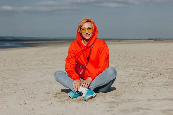Belle fille souriante en sweat à capuche rouge assis sur la plage, saint michaels mount, France — Photo de stock