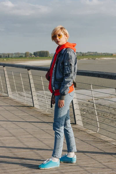 Повний вигляд красивої стильної дівчини в джинсовому одязі і сонцезахисних окулярах, дивлячись на камеру в сонячний день, Мішель, Франція — стокове фото