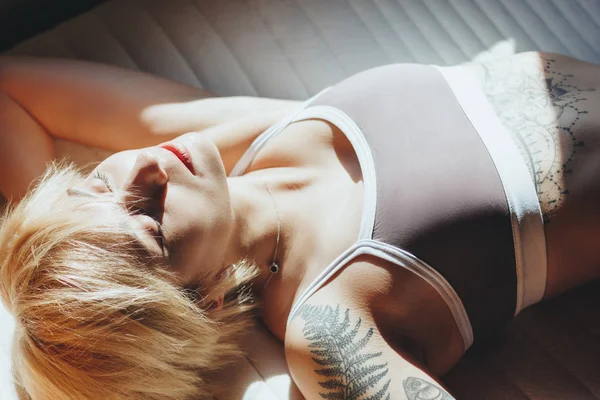 Vista ravvicinata di bella giovane donna con tatuaggi che indossano biancheria intima e riposano alla luce del sole — Foto stock