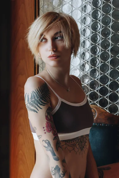 Bela mulher tatuada em roupa interior olhando para longe dentro de casa — Fotografia de Stock