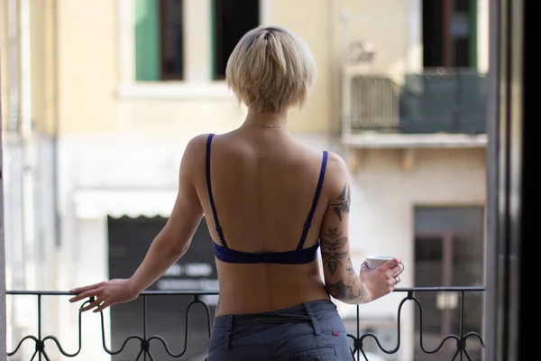 Vista posteriore di giovane donna in reggiseno in possesso di tazza e in piedi sul balcone — Foto stock