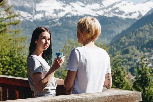 Young women drinking tea and looking at each other while standing on balcony in beautiful mountains, mont blanc, alps — Stock Photo