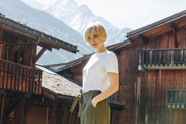Bela feliz jovem mulher olhando para a câmera enquanto de pé com a mão no bolso na aldeia de montanha, mont blanc, alpes — Fotografia de Stock