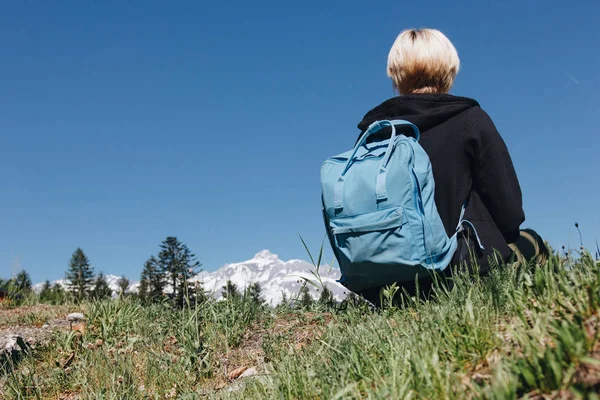 Back view of young female traveler with backpack resting on grass in mountains, mont blanc, alps — Stock Photo