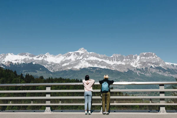 Back view of girls standing near fence and looking at majestic snow-capped mountains, mont blanc, alps — Stock Photo
