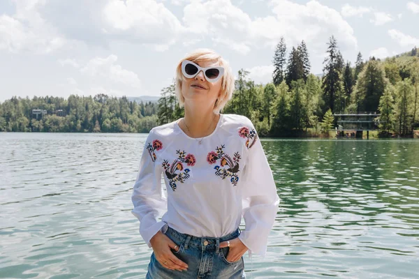 Belle jeune femme en lunettes de soleil debout près pittoresque lac de montagne tranquille, saigné, slovenia — Photo de stock