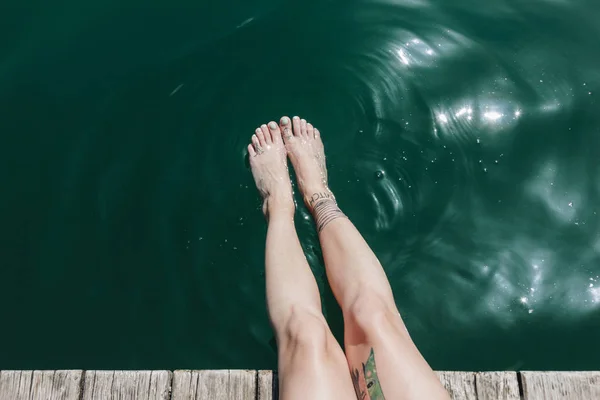 Recortado disparo de piernas femeninas con tatuajes en aguas tranquilas en día soleado — Stock Photo