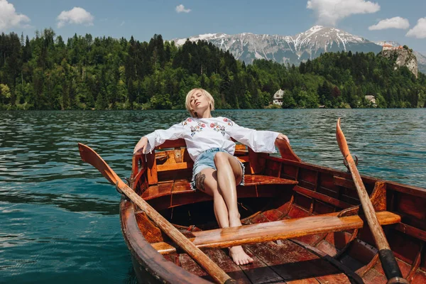 Schöne junge Frau, die sich in einem Boot am ruhigen Bergsee ausruht, blutend, Slowenien — Stockfoto