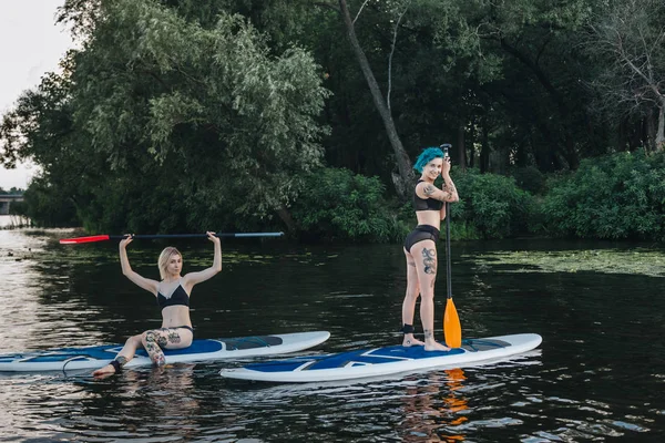 Mujeres atléticas relajarse en tablas de paddle juntos en el río - foto de stock