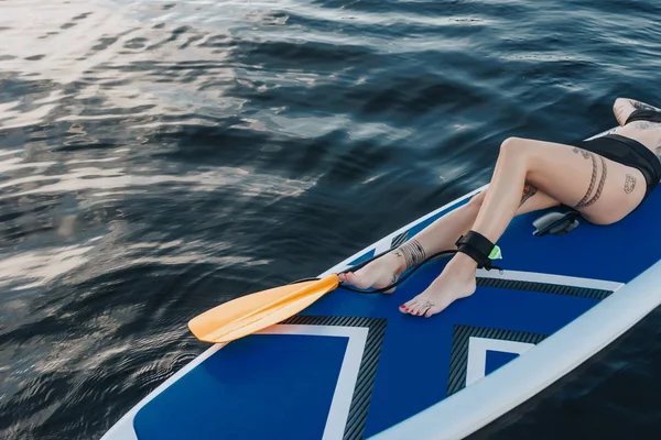 Vista ritagliata di ragazza tatuata rilassante su sup board sul fiume — Foto stock