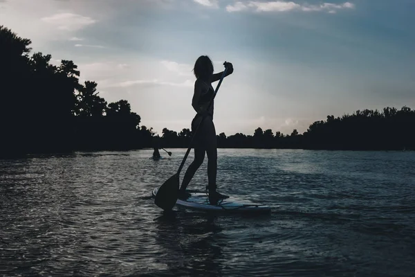 Silhouette of athletic woman standup paddleboarding on river — Stock Photo