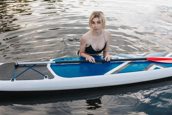 Atractiva chica rubia con tabla de paddle en el agua - foto de stock