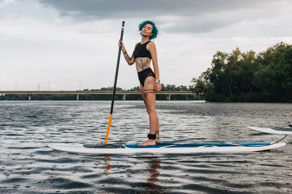 Belle rêveuse sportive tatouée femme standup paddleboard sur la rivière — Photo de stock