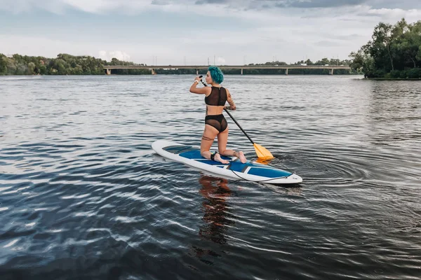 Belle femme tatouée sportive en bikini paddle board sur la rivière — Photo de stock