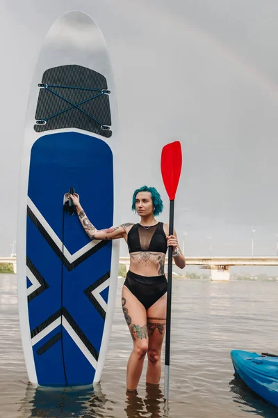 Bela menina atlética posando com paddle board no rio — Fotografia de Stock