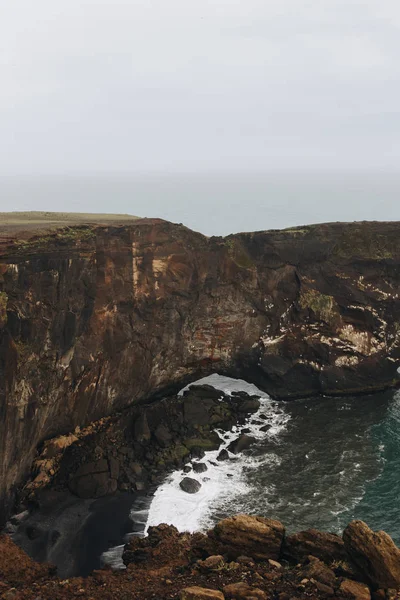 Vista aérea del acantilado rocoso y el océano bajo el cielo nublado en el promontorio Dyrholaey en Vik, Islandia - foto de stock